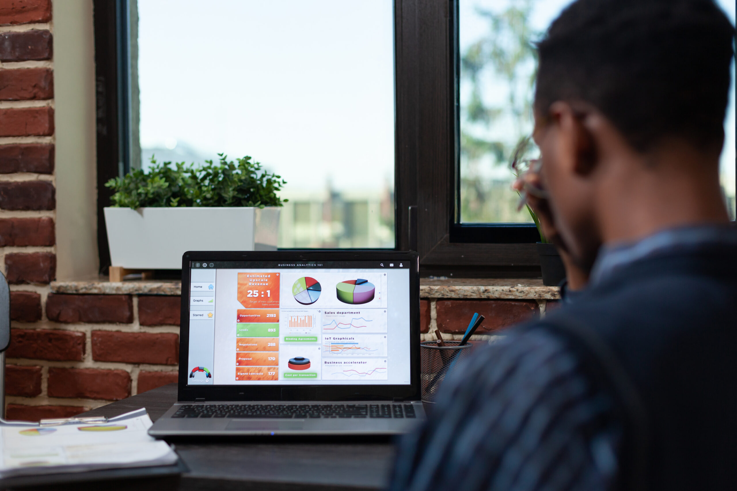Over shoulder view of african american startup employee looking at laptop screen with business analytics charts